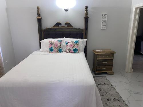 łóżko z białą pościelą i poduszkami oraz stolikiem nocnym w obiekcie MBS Travel Holistic Guest House w mieście Mammee Bay