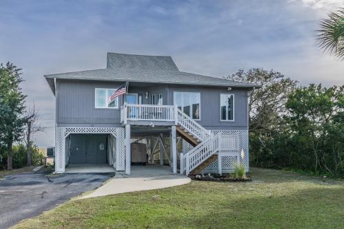 a gray house with a porch and a flag on it at Marsh Views - Nautical Watch - Steps to the Pool in Harbor Island