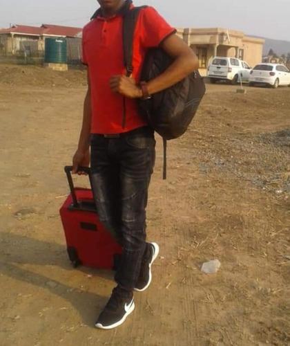 un hombre de pie junto a una maleta roja en SoftLife Capsule Hotel, en Ulundi