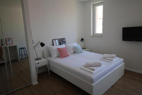 a white bedroom with a bed with pillows and a television at Apartments and Rooms Jospino in Mali Lošinj