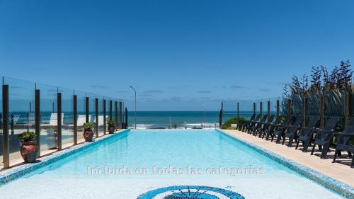 a swimming pool with chairs and the ocean in the background at Hotel AATRAC in Mar del Plata