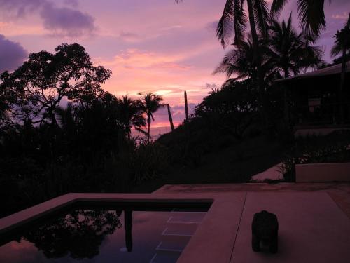 a sunset over a swimming pool and palm trees at Casas Pelicano in Playa Junquillal