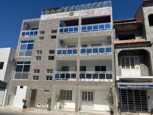 un edificio de apartamentos con ventanas azules en una calle en Hotel Principal en Tarrafal