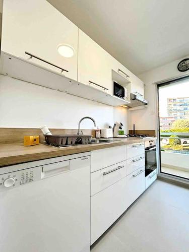une cuisine avec des placards blancs et une grande fenêtre dans l'établissement Le Maeva : Apt 4 Prs, Clim, Garage, piscine, à Antibes