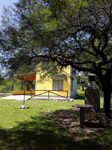 un parque con un árbol y un banco en el césped en Calamuchita Lodges en Villa Rumipal