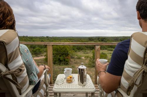 a group of people sitting on a porch looking out at the forest at Simbavati Hilltop Lodge in Timbavati Game Reserve
