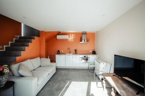 een woonkamer met een witte bank en een oranje muur bij MY House's - 3 maisons avec piscine commune et la maison pour 3 personnes max avec jacuzzi privé 