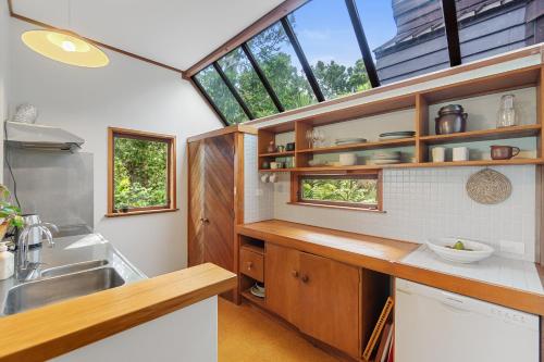 una cocina con armarios de madera, fregadero y ventanas en Treetop Sanctuary - Titirangi Holiday Home en Auckland