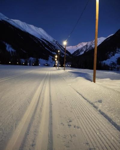 a snow covered street with a light pole and mountains at Apart Alpenflair in Umhausen