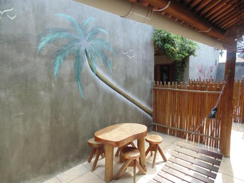 a table and two stools next to a palm tree mural at Chalé Palhano Beach in São Miguel dos Milagres