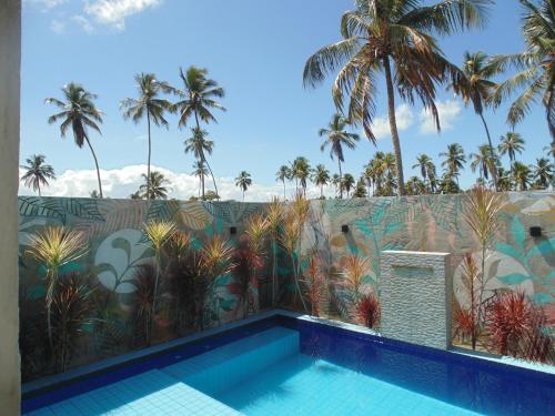 a swimming pool in front of a wall with palm trees at Chalé Palhano Beach in São Miguel dos Milagres