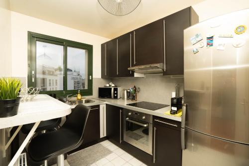 une cuisine avec des armoires noires et un réfrigérateur en acier inoxydable dans l'établissement Studio cosy - Asnières, à Asnières-sur-Seine