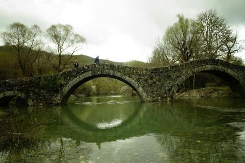 a stone bridge over a river with people walking on it at Βίτσα Πετρόκτιστο Αρχοντικό "Ιόλη" με θέα Ζαγόρι in Vitsa