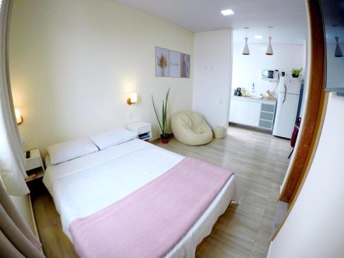 a bedroom with a white bed and a kitchen at Suítes do Cabo in Arraial do Cabo