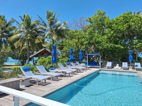 a group of chairs and a swimming pool with blue umbrellas at Beach House Lodge in Poum