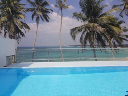 a swimming pool with palm trees and the ocean at Cool Beach Hotel in Hikkaduwa