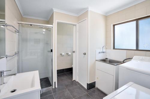 La salle de bains blanche est pourvue d'un lavabo et d'une douche. dans l'établissement Gold Rush Apartments, à Gympie