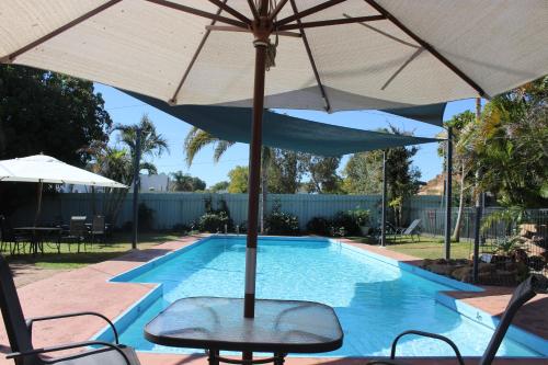 an umbrella and chairs next to a swimming pool at Mt Isa Caravan Park in Mount Isa
