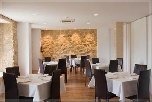 un restaurante con mesas y sillas blancas y una pared de piedra en Hostal Doña Blanca, en Sigüenza