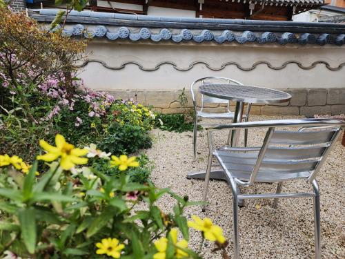 two chairs and a table in a garden with flowers at Jahayeon Hanokstay in Jeonju