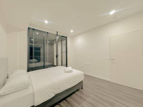 a white bedroom with a bed and a large mirror at Burwood Cozy Apartment Free Parking in Sydney