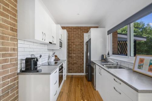 a kitchen with white cabinets and a brick wall at Bluestone Cottage - Character & Class in Orange