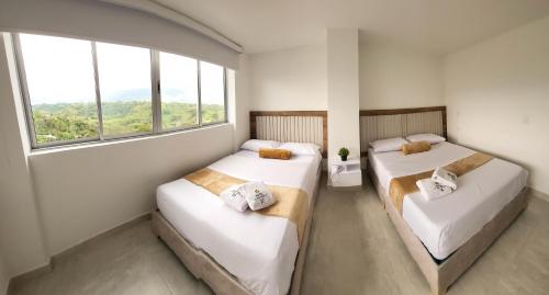 two beds in a room with two windows at Hotel La Gran Estaciónag in Armenia