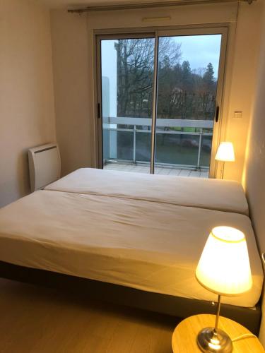 un lit dans une chambre avec une grande fenêtre dans l'établissement T2 lumineux avec balcon et parking, à Bagnoles-de-l'Orne