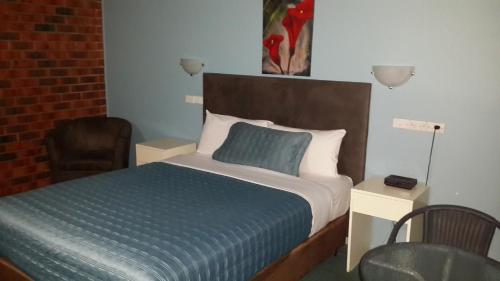a bedroom with a bed with a blue blanket and a chair at Zero Inn Motel in Nhill