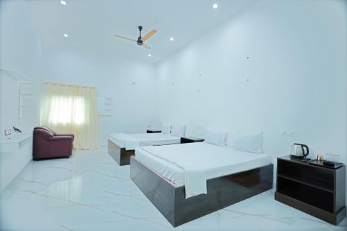 een witte kamer met 2 bedden en een stoel bij LK.Lodge in Kanyakumari