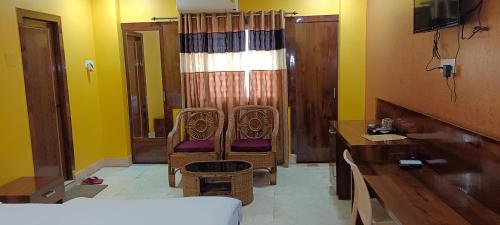 een kamer met 2 stoelen, een bureau en een bed bij New Hindusthan Hotel in Siliguri