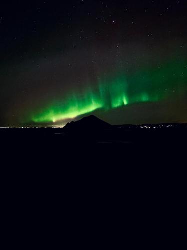 an aurora in the sky over a mountain at Eyja Mork - Aurora Dome with Private Bathroom and other facilities in Hvolsvöllur