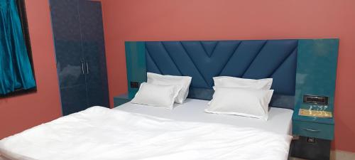 een bed met een blauw hoofdeinde en witte kussens bij New Hindusthan Hotel in Siliguri