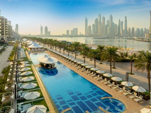 ドバイにあるMarriott Resort Palm Jumeirah, Dubaiの傘とヤシの木と街のプールを併設しています。