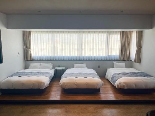 three beds in a room with a window at ゆくれば前島ホテル in Naha