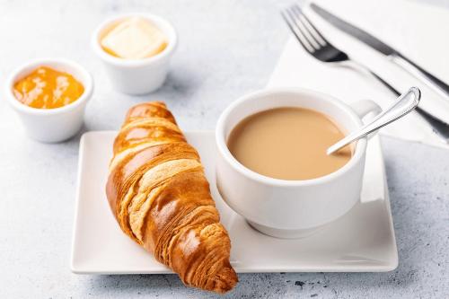 a cup of coffee and a croissant on a plate at THE REJOICE VENTURE in Gurgaon