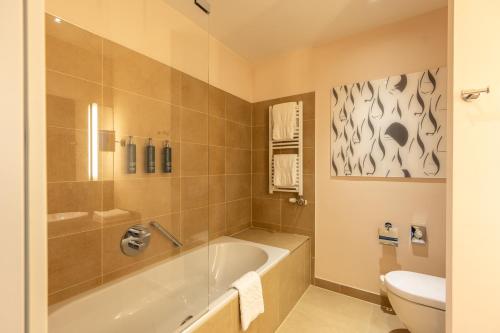 ein Bad mit einer Badewanne und einem WC in der Unterkunft DoubleTree by Hilton Oradea in Oradea