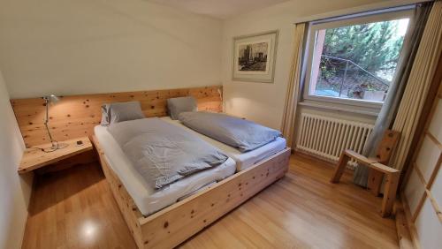 een slaapkamer met een houten bed en een raam bij Chesa Bellaval, Haus Leivra 2-Zimmerwohnung in Silvaplana
