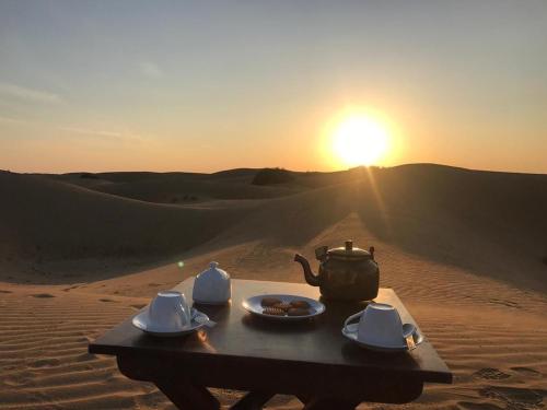 a table with a tea set in the desert with the sunset at Jaisal heritage desert camp in Jaisalmer