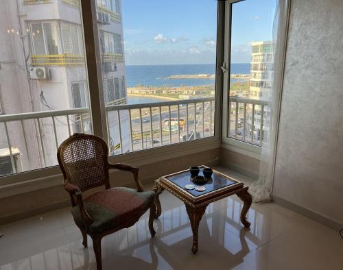 een kamer met een stoel, een tafel en een raam bij Sea View Luxury Apartment in Alexandrië