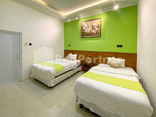 two beds in a room with a green wall at CBG INN RedPartner near Stasiun Solo Balapan in Kadiporo