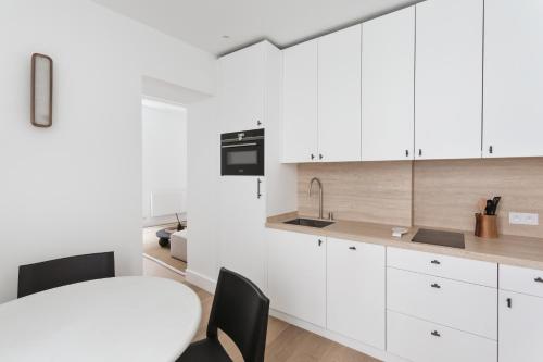 une cuisine avec des armoires blanches et une table et des chaises dans l'établissement Adresse Prestigieuse: Appartement Luxueux Marais, à Paris