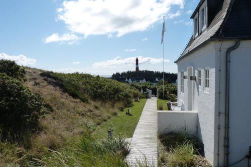 a pathway leading to a building with a lighthouse in the background at Haidewai in Hörnum