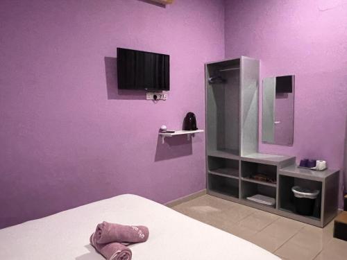 Habitación púrpura con cama y TV en la pared. en OYO 90907 Brick Cottage Homes en Kuah