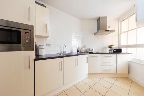 a white kitchen with white cabinets and a microwave at Bond Street Apartment - Sleeps 4 in London