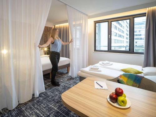 Novotel Suites Wien City Donau في فيينا: امرأة تقف في غرفة الفندق وتطل على النافذة