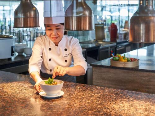 Uma mulher na cozinha a preparar comida numa tigela. em Novotel Phu Quoc Resort em Phu Quoc