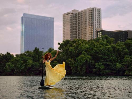 Una donna con un vestito giallo su una tavola da surf in acqua di Fairmont Austin ad Austin