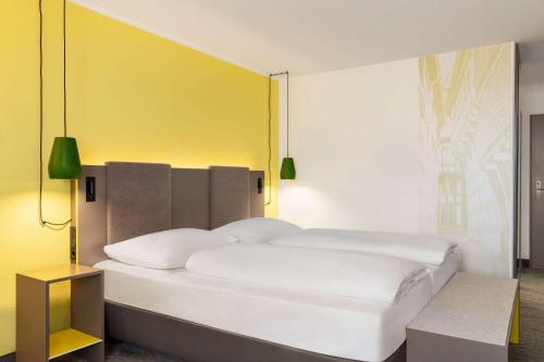 a bedroom with a white bed with a yellow wall at Vienna House Easy by Wyndham Limburg in Limburg an der Lahn