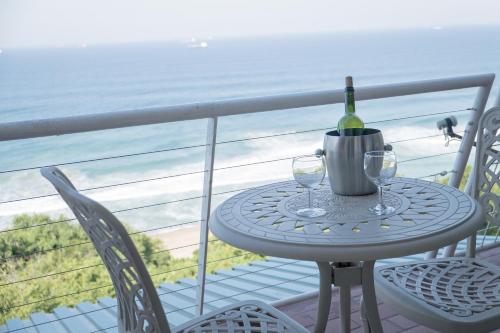 a table with a bottle of wine and two glasses on a balcony at Sands Beach Breaks Umdloti Beach View in Umdloti